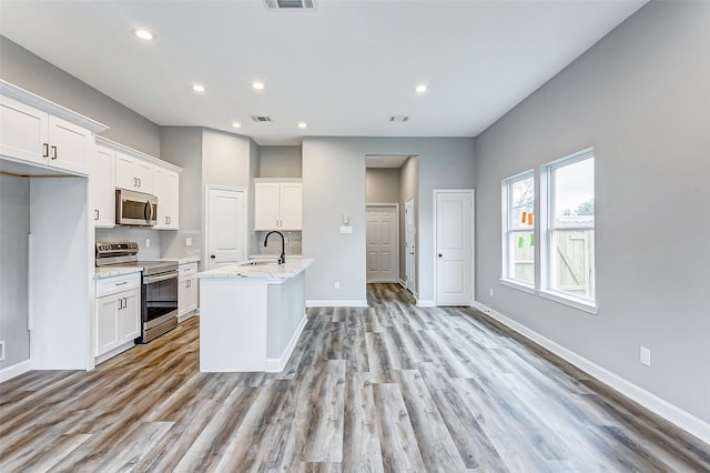 kitchen featuring light wood-type flooring, appliances with stainless steel finishes, light stone counters, and white cabinets