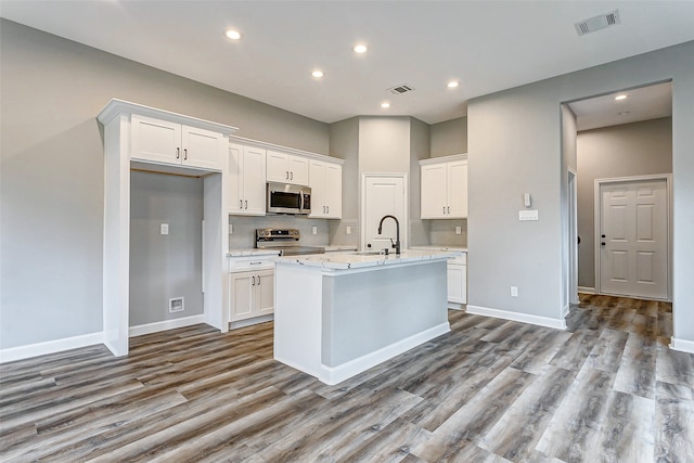 kitchen featuring appliances with stainless steel finishes, white cabinetry, a center island with sink, and light hardwood / wood-style floors