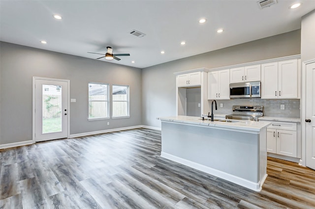 kitchen featuring hardwood / wood-style floors, appliances with stainless steel finishes, white cabinetry, ceiling fan, and a kitchen island with sink