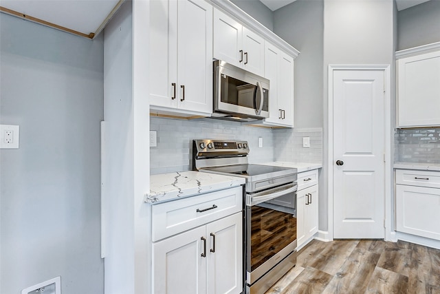 kitchen with light wood-type flooring, appliances with stainless steel finishes, backsplash, and white cabinetry