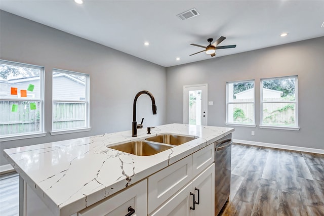 kitchen with a kitchen island with sink, white cabinetry, hardwood / wood-style flooring, ceiling fan, and light stone counters