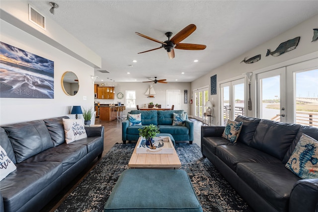 living room with a textured ceiling, french doors, dark colored carpet, and ceiling fan