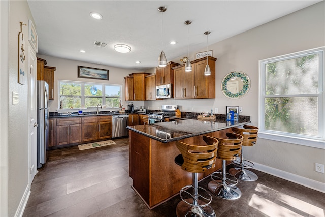 kitchen with decorative light fixtures, stainless steel appliances, dark stone countertops, a kitchen bar, and kitchen peninsula