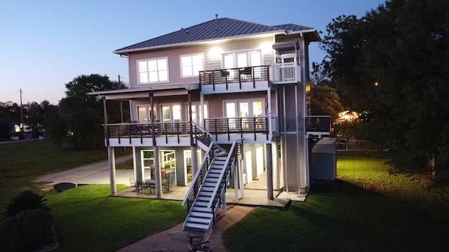 back house at dusk featuring a balcony, a patio area, and a yard