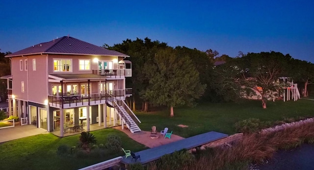 back house at twilight with a balcony, a patio area, and a yard