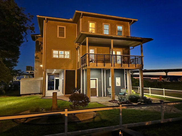 back house at twilight with a balcony and a lawn