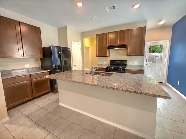 kitchen featuring light stone counters, sink, an island with sink, and black appliances