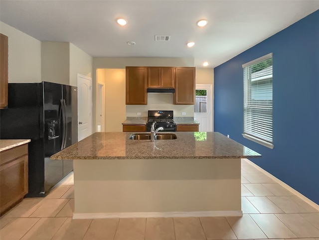 kitchen featuring light tile flooring, black appliances, a kitchen island with sink, dark stone countertops, and sink