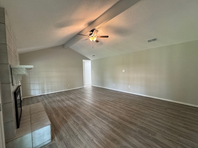 unfurnished living room with ceiling fan, vaulted ceiling with beams, a fireplace, dark wood-type flooring, and a textured ceiling