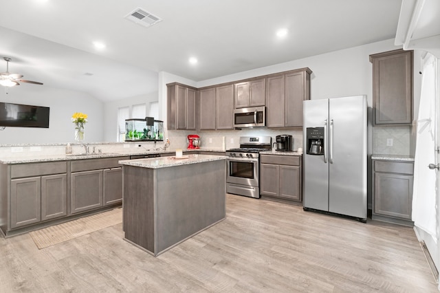 kitchen with light stone countertops, kitchen peninsula, appliances with stainless steel finishes, light hardwood / wood-style flooring, and ceiling fan