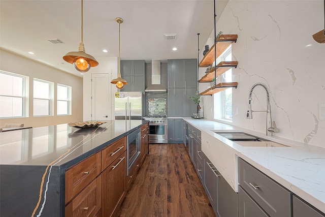 kitchen featuring pendant lighting, wall chimney range hood, sink, light stone countertops, and appliances with stainless steel finishes