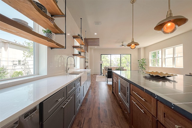 kitchen with ceiling fan, stainless steel microwave, sink, hanging light fixtures, and dark hardwood / wood-style flooring