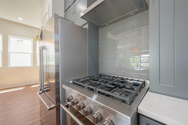 kitchen with gray cabinetry, high quality appliances, wall chimney range hood, and backsplash