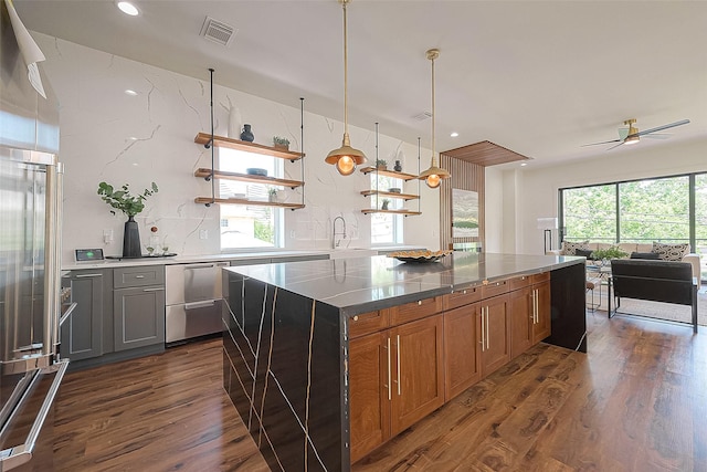 kitchen featuring ceiling fan, decorative light fixtures, dark stone countertops, dark hardwood / wood-style floors, and a kitchen island