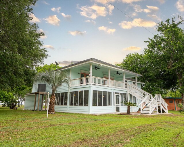 back house at dusk featuring a lawn, ceiling fan, a balcony, and a sunroom