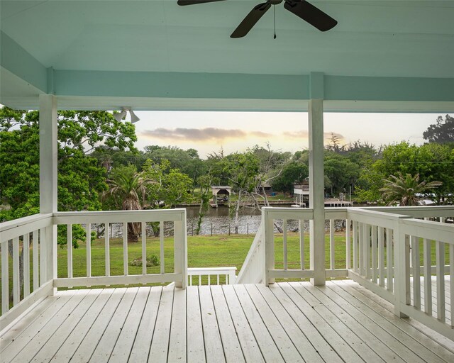 deck at dusk with ceiling fan, a yard, and a water view