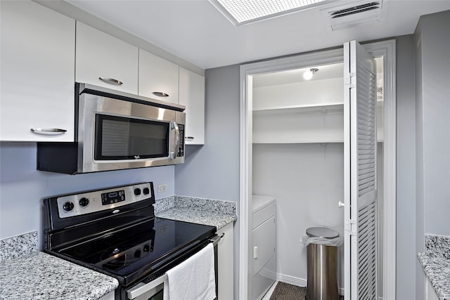 kitchen with appliances with stainless steel finishes, light stone countertops, washer / dryer, and white cabinetry