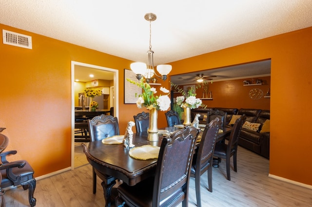 dining space with ceiling fan with notable chandelier, a textured ceiling, and hardwood / wood-style floors