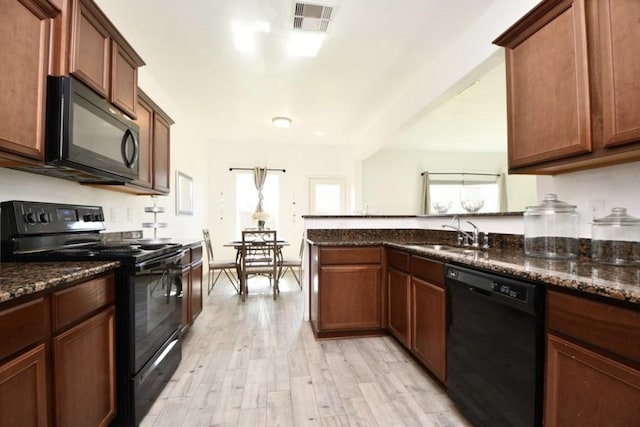 kitchen with sink, black appliances, a barn door, dark stone countertops, and light hardwood / wood-style floors