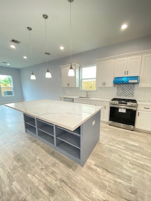 kitchen featuring white cabinets, decorative light fixtures, a kitchen island, and stainless steel range oven