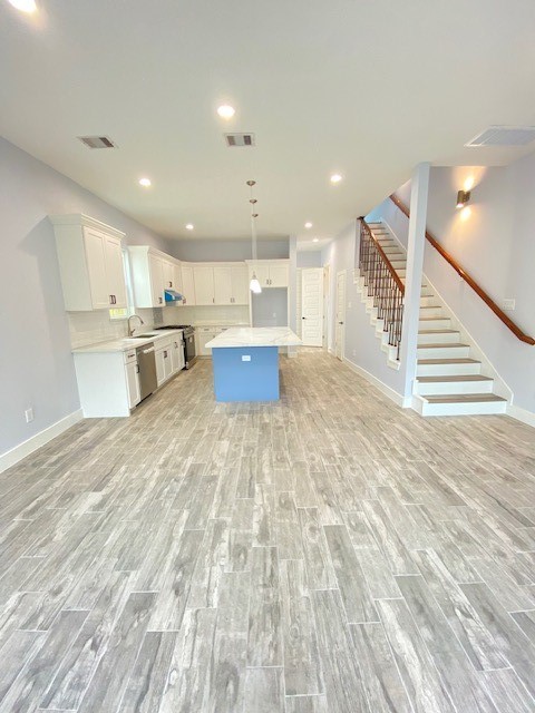 kitchen with white cabinetry, stainless steel appliances, pendant lighting, light hardwood / wood-style floors, and a kitchen island