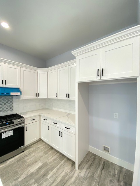 kitchen with tasteful backsplash, white cabinetry, stainless steel range, and light stone counters