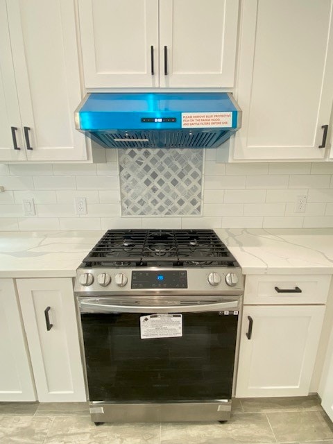 kitchen with gas stove, light stone countertops, wall chimney range hood, backsplash, and white cabinets