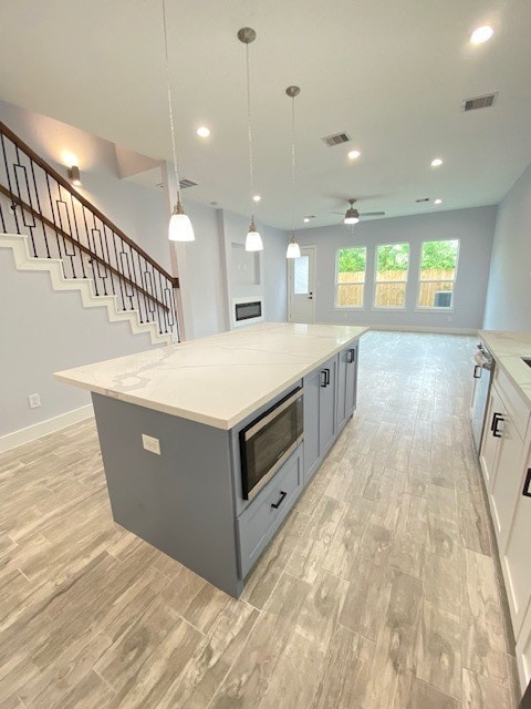 kitchen with light stone counters, a spacious island, decorative light fixtures, white cabinets, and stainless steel microwave