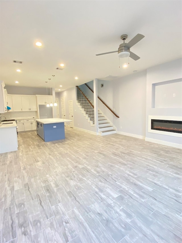 unfurnished living room with light wood-type flooring, ceiling fan, and sink