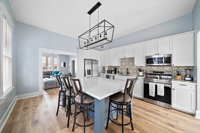 kitchen featuring appliances with stainless steel finishes, light hardwood / wood-style flooring, hanging light fixtures, tasteful backsplash, and white cabinets