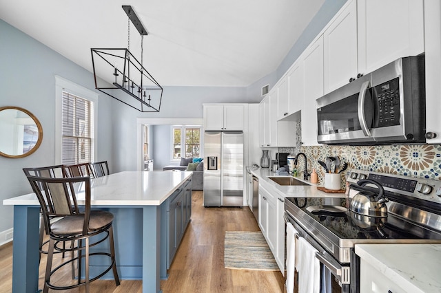 kitchen featuring a kitchen bar, backsplash, stainless steel appliances, white cabinetry, and light wood-type flooring