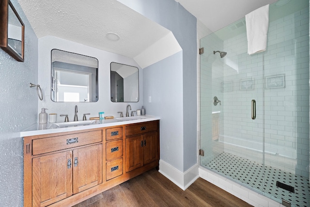 bathroom with a textured ceiling, an enclosed shower, dual bowl vanity, and hardwood / wood-style flooring