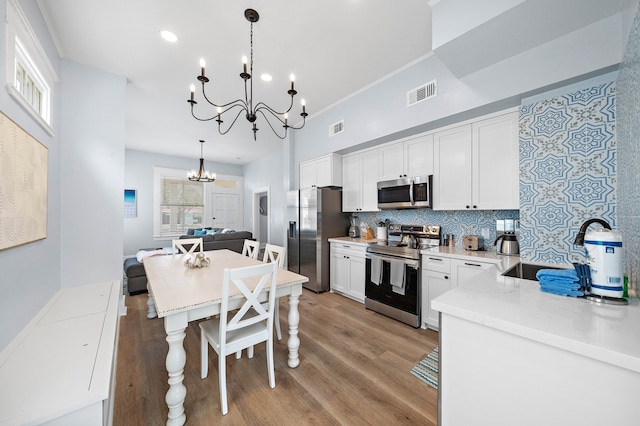 kitchen featuring pendant lighting, appliances with stainless steel finishes, white cabinets, and a notable chandelier