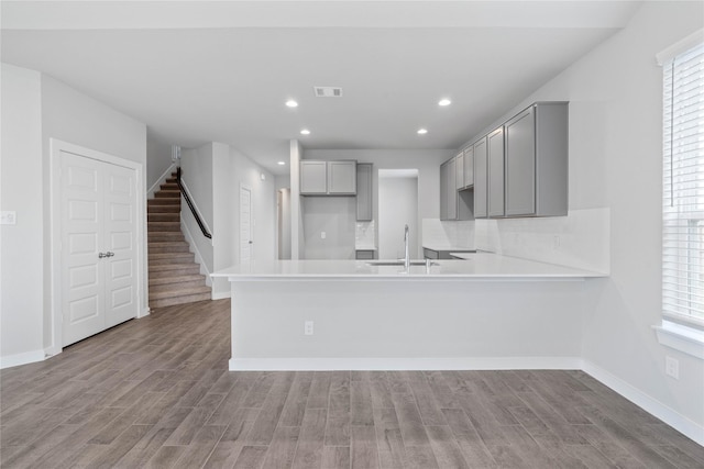 kitchen featuring gray cabinetry, sink, kitchen peninsula, decorative backsplash, and light wood-type flooring