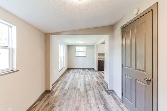 hall with lofted ceiling, light wood-type flooring, and a textured ceiling