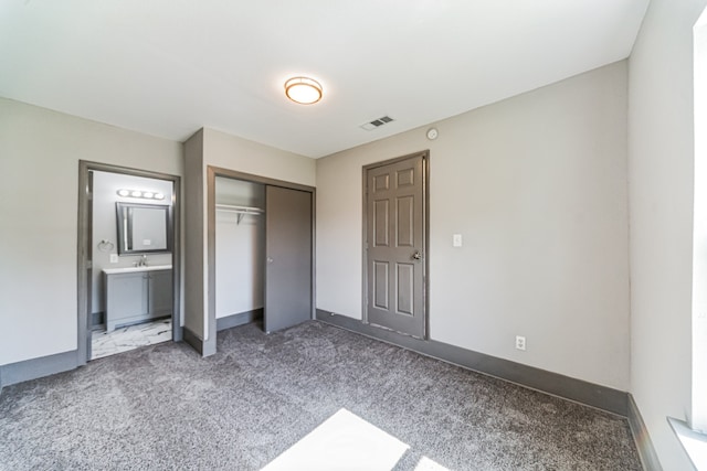 unfurnished bedroom featuring a closet, sink, ensuite bathroom, and carpet floors