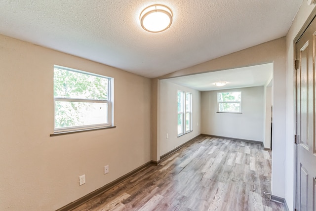 empty room with vaulted ceiling, a textured ceiling, and hardwood / wood-style floors