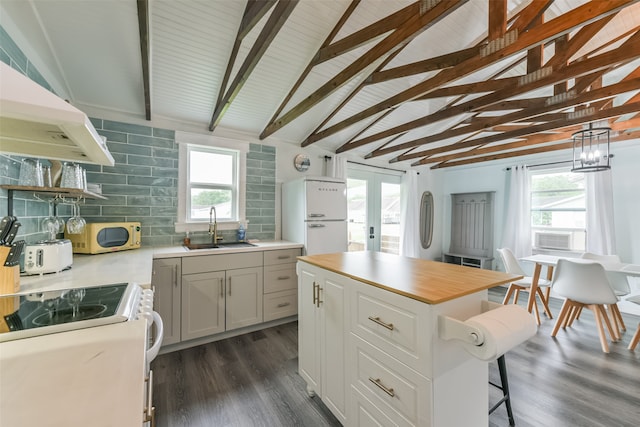 kitchen with white appliances, vaulted ceiling with beams, dark wood-type flooring, sink, and a center island