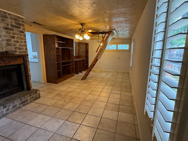 unfurnished living room featuring ceiling fan, brick wall, a textured ceiling, a fireplace, and light tile floors