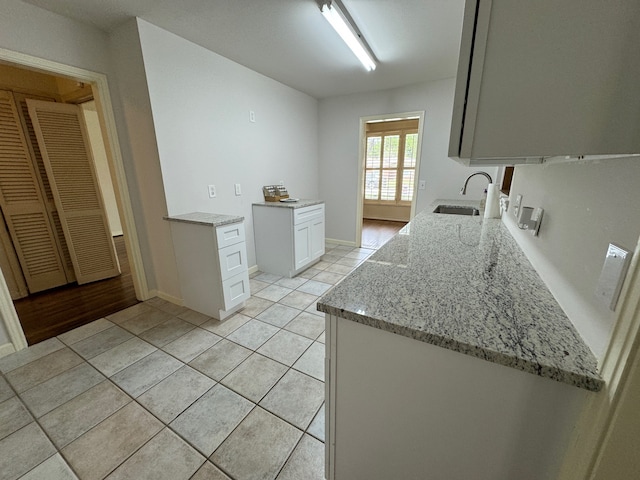 kitchen featuring sink, white cabinetry, light tile floors, and light stone countertops