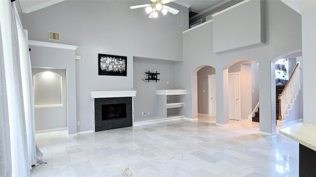 unfurnished living room featuring ceiling fan, ornamental molding, and a high ceiling