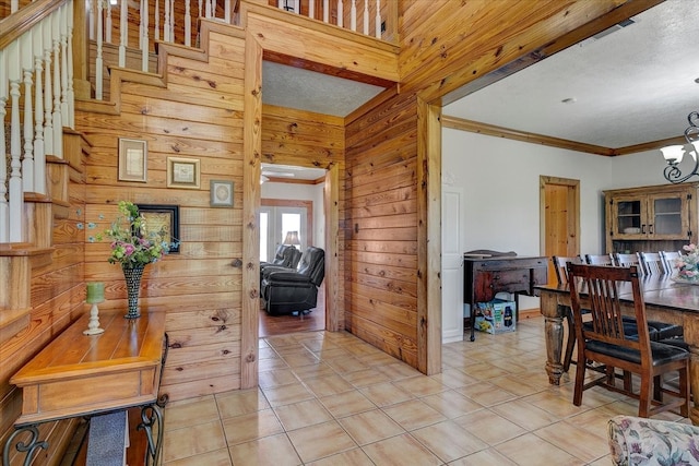 interior space with ornamental molding, a notable chandelier, wood walls, and a textured ceiling