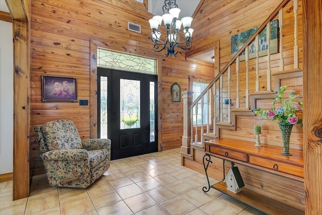 tiled foyer entrance with high vaulted ceiling, wood walls, and an inviting chandelier