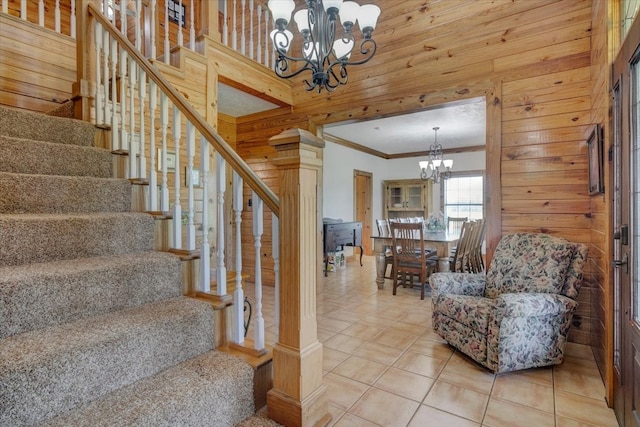 stairs with a notable chandelier, wood walls, crown molding, and light tile flooring