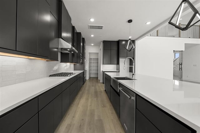 kitchen with light wood-type flooring, stainless steel appliances, decorative light fixtures, and sink