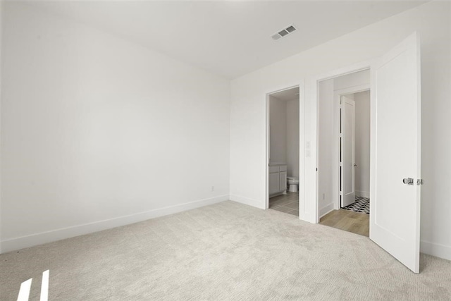 unfurnished bedroom featuring light carpet and ensuite bath