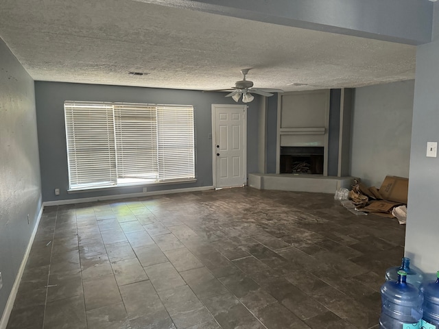 unfurnished living room featuring ceiling fan, dark tile floors, and a textured ceiling