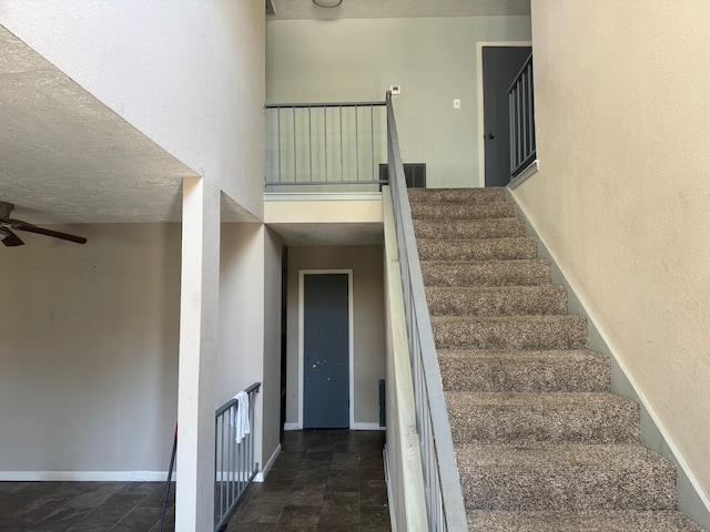 stairs with a textured ceiling, ceiling fan, a towering ceiling, and dark tile floors