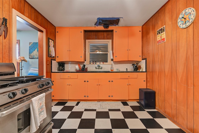 kitchen featuring dark tile flooring, tasteful backsplash, stainless steel gas stove, and wood walls