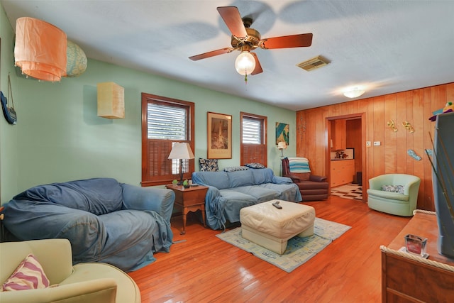 living room with light hardwood / wood-style flooring, wood walls, and ceiling fan